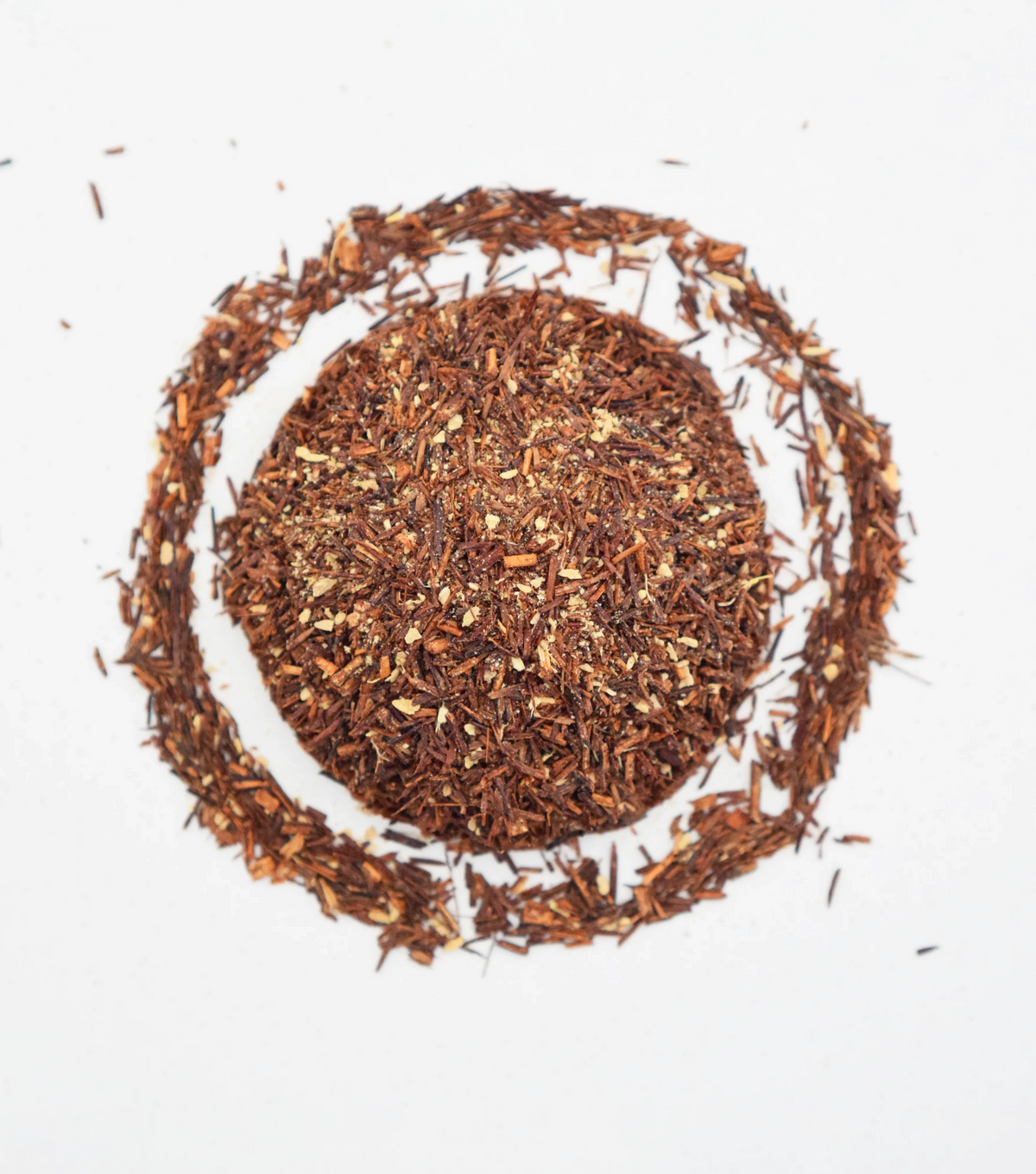 Organic loose-leaf Rooibos ginger tea in a circular heap with scattered tea leaves on white background