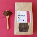 Rooibos Tea package with a wooden spoon full of Rooibos tea leaves on a pink background
