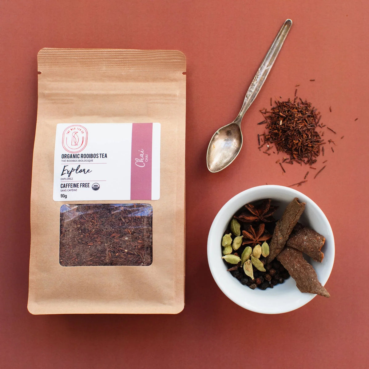 90g bag of organic Rooibos Chai tea with loose Rooibos and chai spices including cardamom, star anise, and cinnamon on rust background