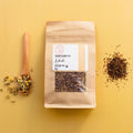 Rooibos Tea package with a wooden spoon and Rooibos tea and Chamomile flowers on a yellow background