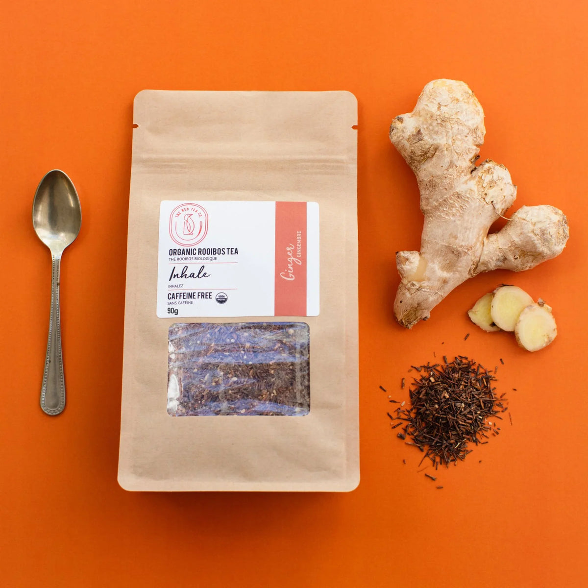 Organic Rooibos Ginger tea package with ginger root, loose rooibos tea, and a spoon on orange background