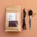 Rooibos Tea package with Rooibos tea leaves and vanilla beans and a spoon on a peach background