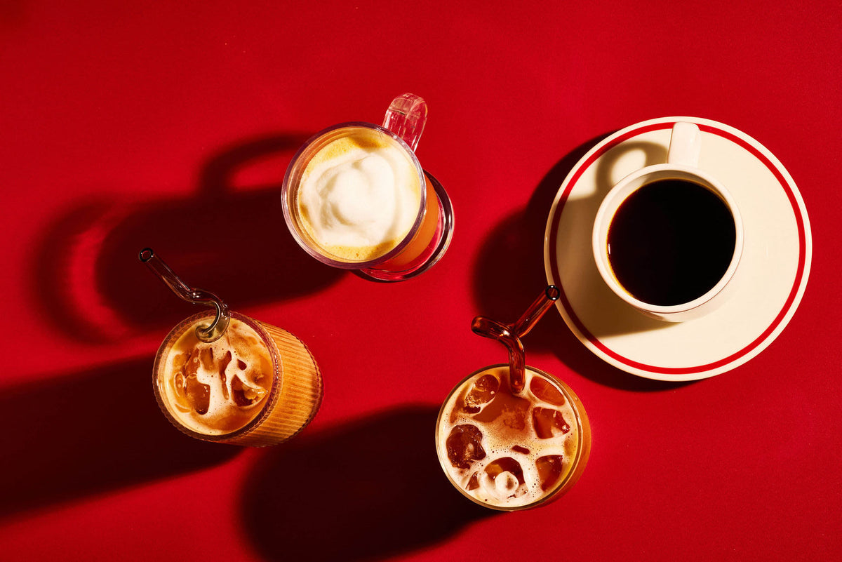 Three glasses of coffee and a cup of black coffee on a saucer arranged on a bright red background with dramatic shadows.