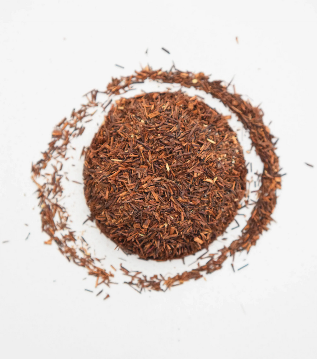 Organic loose-leaf Rooibos chai long cut tea arranged in a circular shape on white background